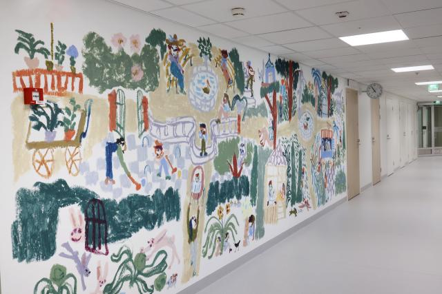 Marika Maijala: Piilosilla, 2023. Kuva: Heli Nukki Sairaalan käytävän seinässä yksityiskohtainen maalaus, jossa eri hahmot viettävät aikaa puistossa.